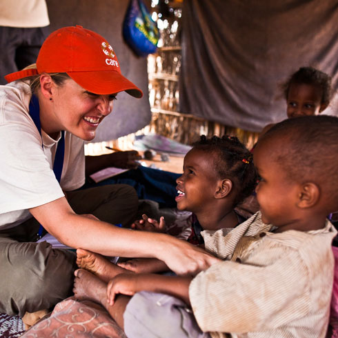 Des enfants des bidonvilles sont assis avec une employée CARE dans une tente et sourient