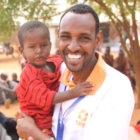 Un homme sourit en regardant l'appareil photo et tiens un enfant dans ses bras.