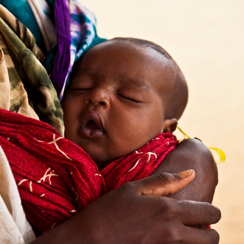 Un bébé dort dans les bras de sa mère.