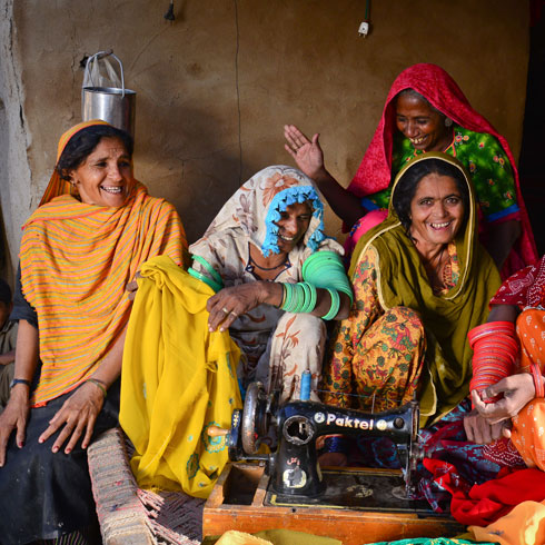 Des femmes sont assises derrière une machien à coudre et rigolent. 