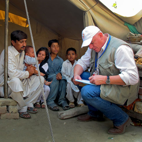 Un collaborteur de CARE est assis parmi une famille et  note quelque chose sur un bout de papier. sammen und notiert etwas auf einen Zettel.
